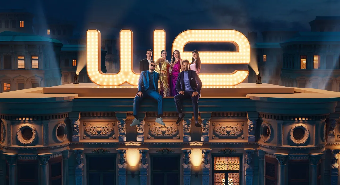 WE campaign scene with three women seated in front of a huge illuminated WE sign above a city building