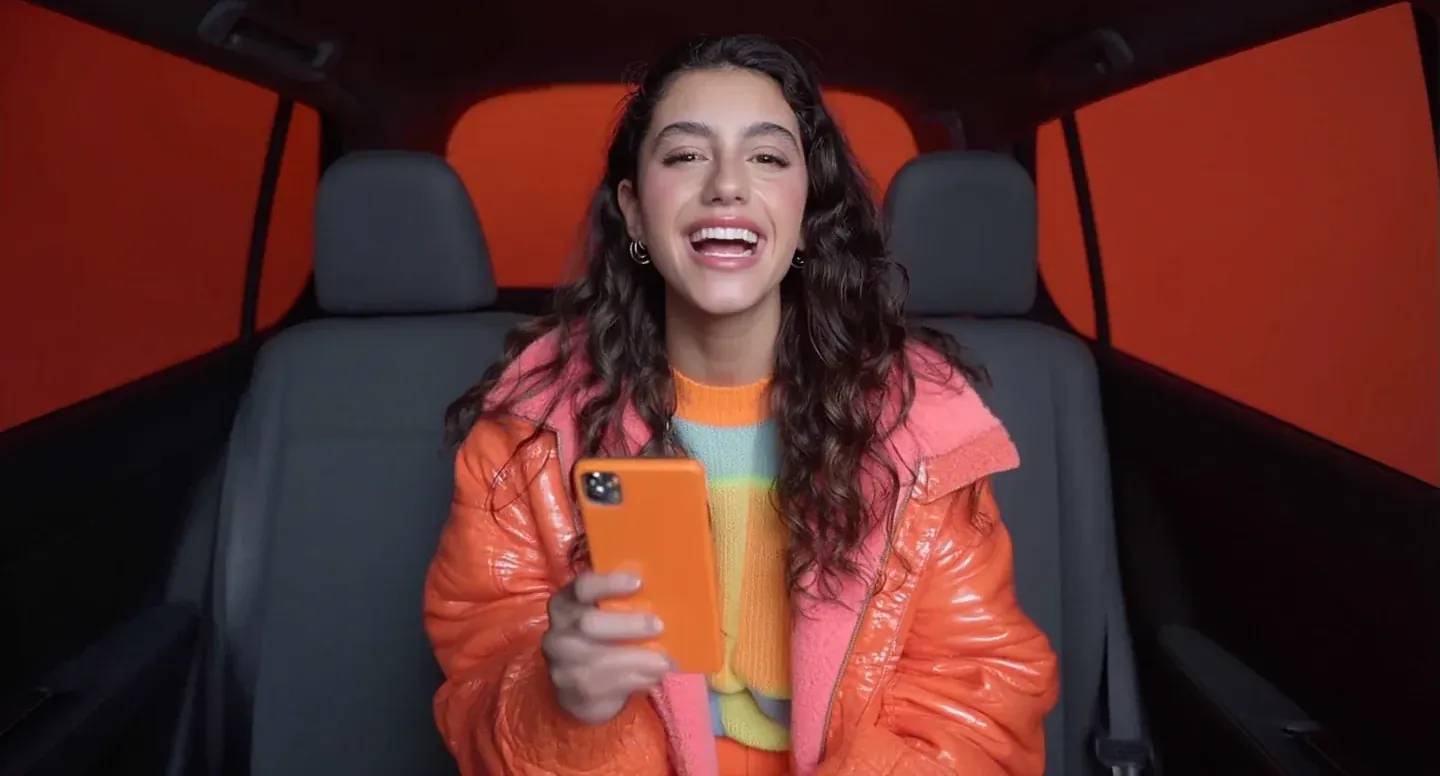 DiDi supplied AI storyboard frame of a smiling woman holding a phone in the back of a car